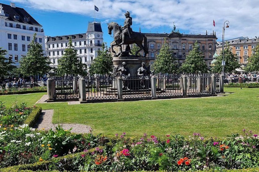 A statue of a horse and rider in a park with buildings in the background. 3