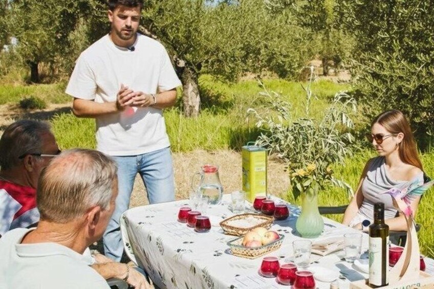 A group of people around a table with food and drinks, outdoors with trees and greenery. 1