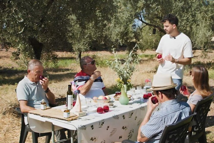 A group of people dining outdoors at a table with a floral tablecloth, surrounded by trees. 1