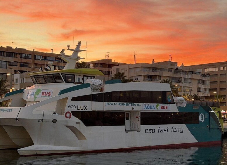 A ferry with 'eco LUX' and 'AQUA BUS' branding, docked at a port with buildings in the background during sunset. 2