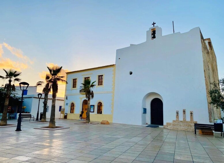 A white building with a cross on top, palm trees, and a tiled plaza. 3