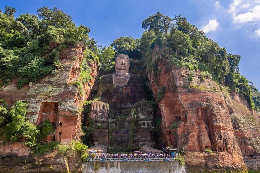 Eine große Felsformation mit einem in Stein gemeißelten Gesicht, umgeben von üppiger Vegetation und einem Fluss darunter. 2