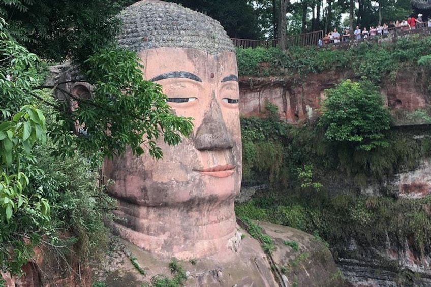 Eine große Buddha-Statue, umgeben von üppigem Grün und einer steilen Felswand. 3