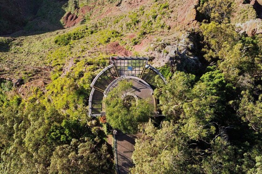 Una piattaforma panoramica circolare con tetto in vetro, immersa in fitta vegetazione e terreno roccioso. 4