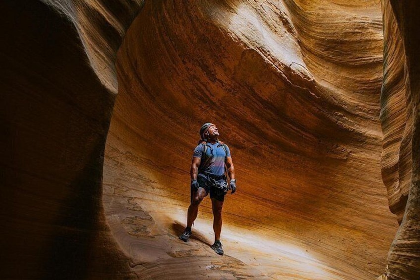 Une personne se tient debout dans un canyon étroit, bordé de parois rocheuses lisses, de couleur rouge-brun. 2