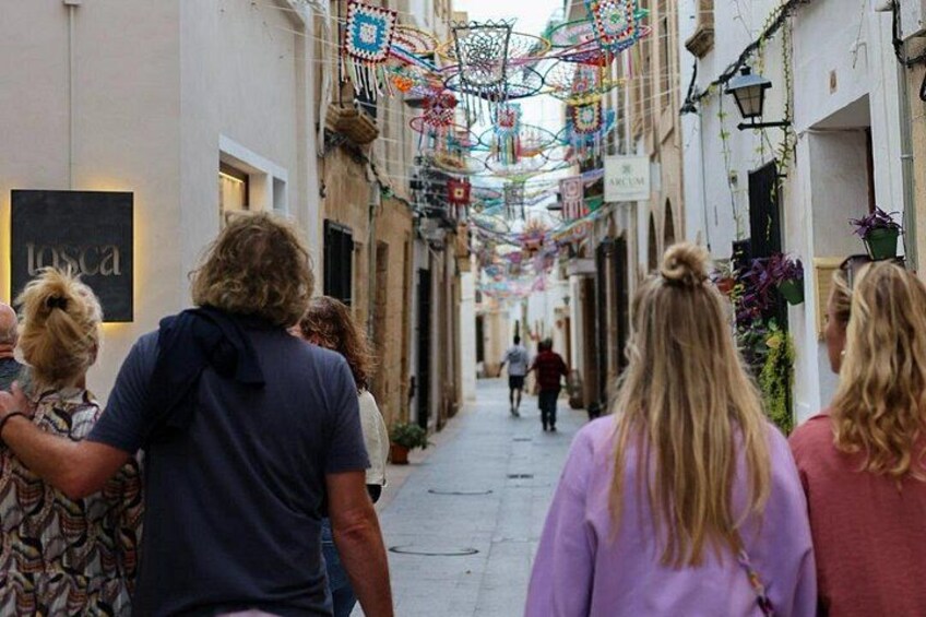 A narrow street with people walking, overhead decorations, and shop signs. 5