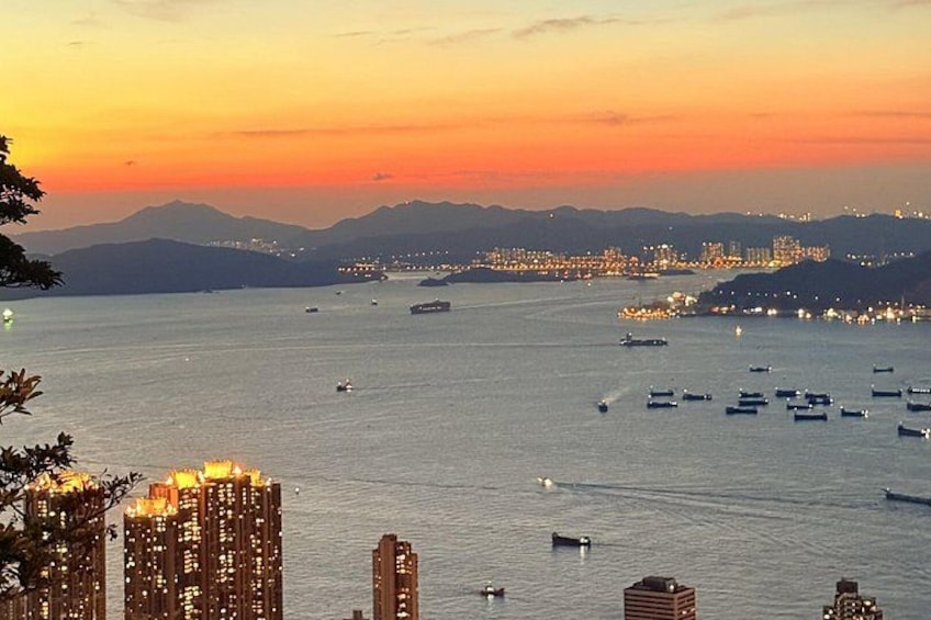 A sunset over a body of water with boats, city lights, and distant mountains. 4
