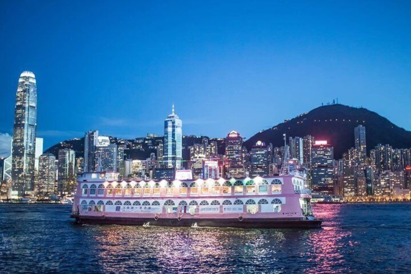 A river cruise boat with a pink and white color scheme, a large dome structure on the deck, and a city skyline with high-rise buildings and a hill in the background. 3