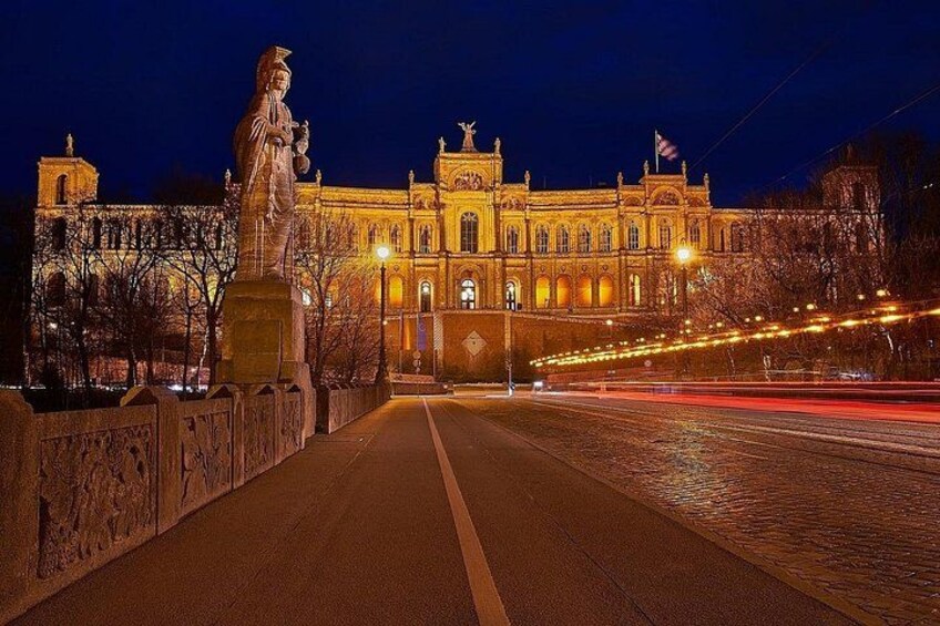 A grand building with classical architecture, a statue on a bridge, and a well-lit street. 2