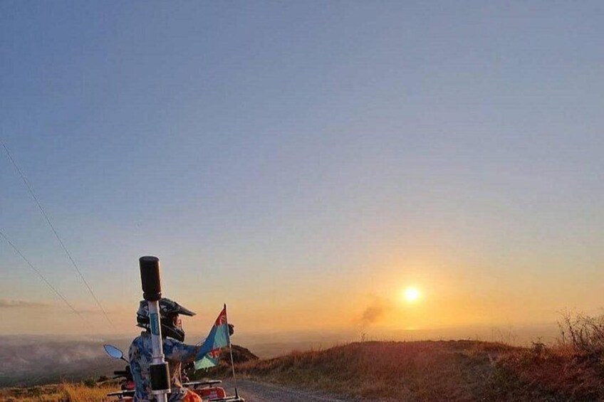 Tramonto su un paesaggio collinare, con un veicolo e una bandiera a sinistra. 1