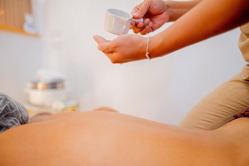 A person receiving a massage with a cup of liquid being poured onto their back. 1