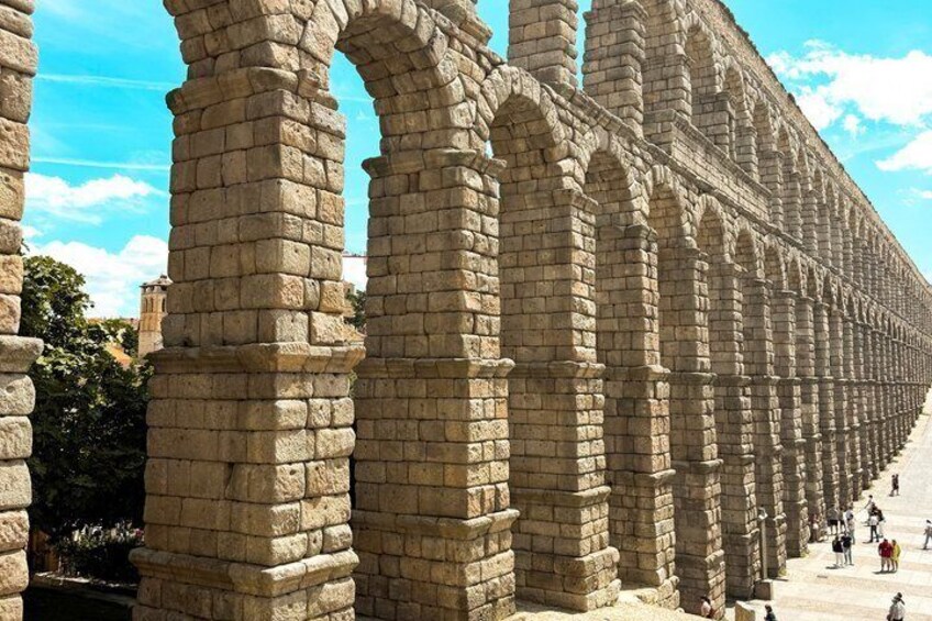 Ancient stone arches, a clear sky, and a pathway with people. 2