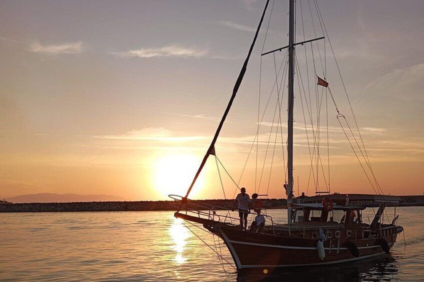 A boat with a mast and sails, docked at sunset with the sun low on the horizon. 3