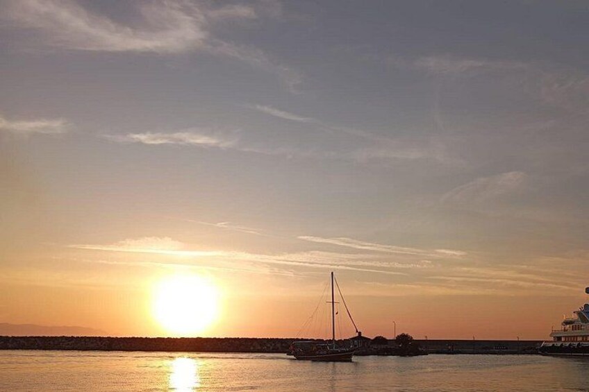 A sunset over a calm body of water with a boat and a pier in the foreground. 2