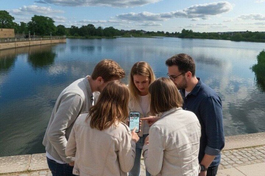 A group of people standing by a calm river, some looking at a smartphone. 4