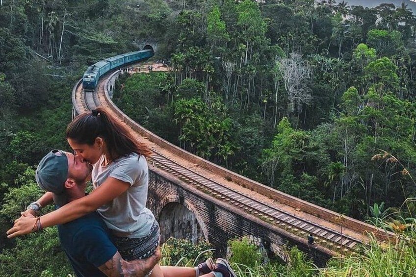 Una pareja se abraza sobre una vía de tren curva rodeada de abundante vegetación. 1