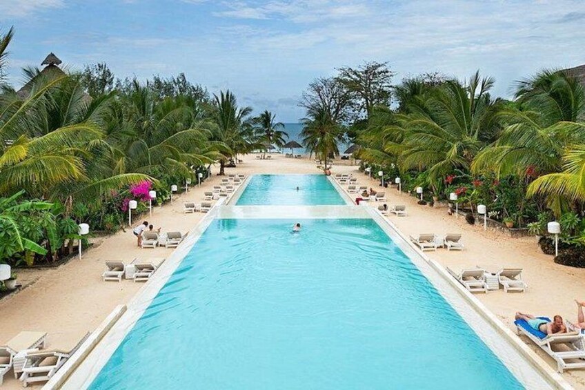 A pool with lounge chairs, palm trees, and a beach. 3