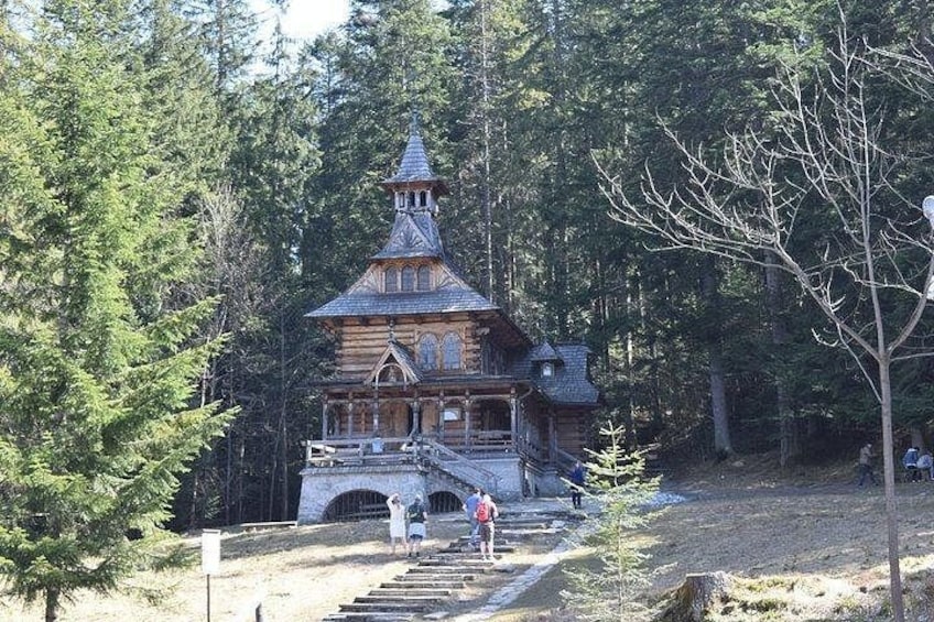 Een houten chalet met een hellend dak en een toren, omgeven door dicht bos. 4