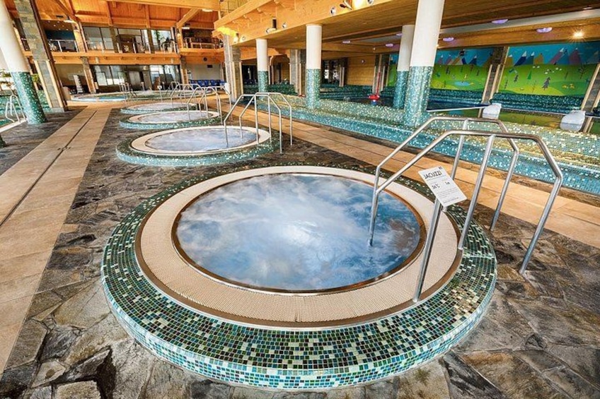 Een groot overdekt zwembad met meerdere whirlpools, omringd door mozaïektegels en stenen vloeren. 2