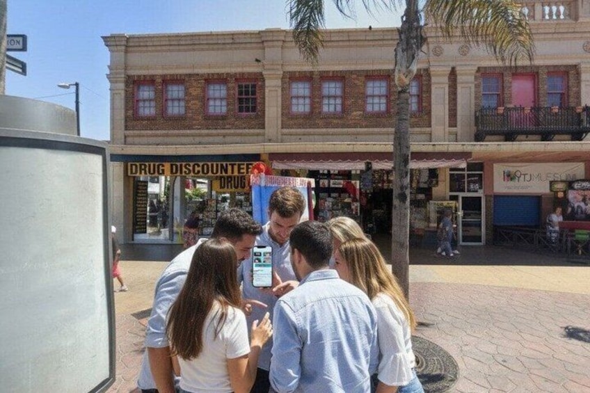 A group of people gathered around a man in front of a building with a sign that reads 'DRUG DISCOUNTER.' 1