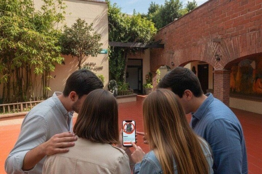 A group of people looking at a smartphone, standing in an outdoor area with brick architecture and greenery. 3