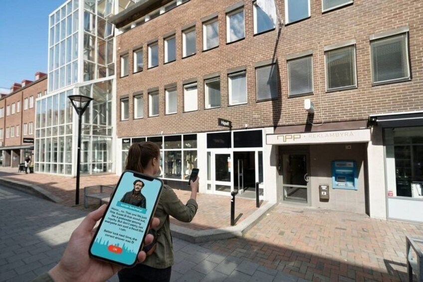 A person holding a smartphone with a map application, standing in front of a building with a glass facade and a sign that reads 'NPP - REKLAMBYRA'. 4