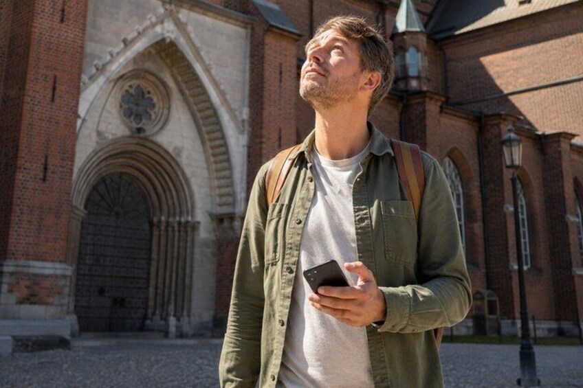 A person standing in front of a historic building with arched windows and a large door. 5