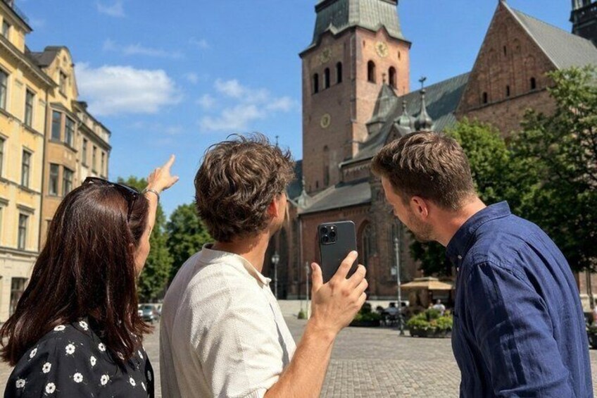 Three people standing outdoors, one pointing at a building with a clock tower. 1