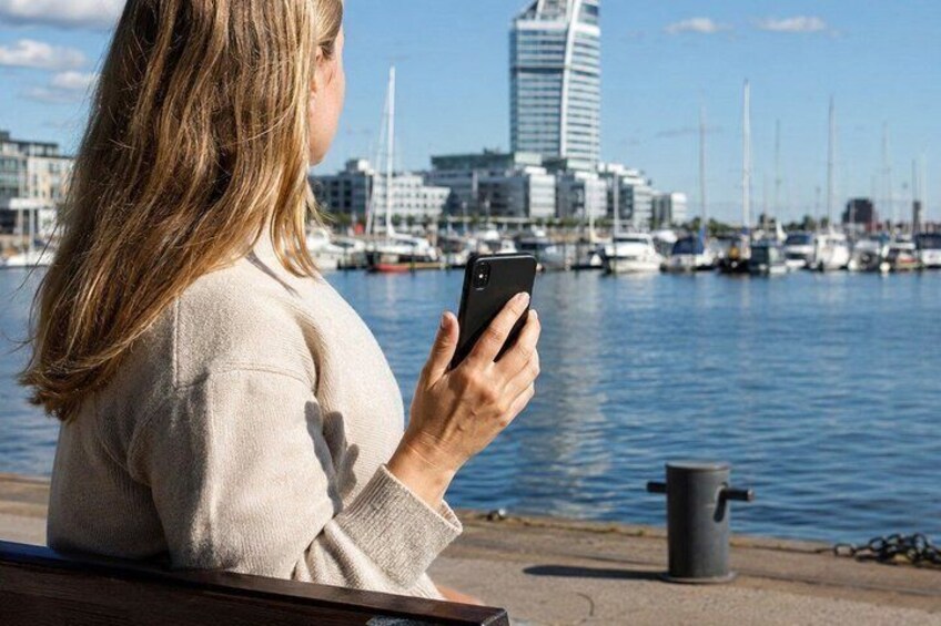 A person sitting by a waterfront, holding a smartphone. 2