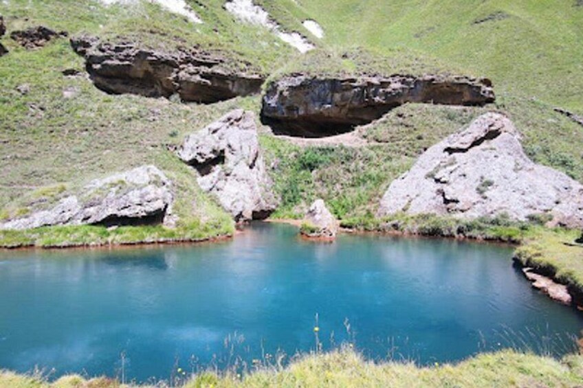 Ein klarer, blauer See, umgeben von felsigem Gelände und grünen Hügeln. 4