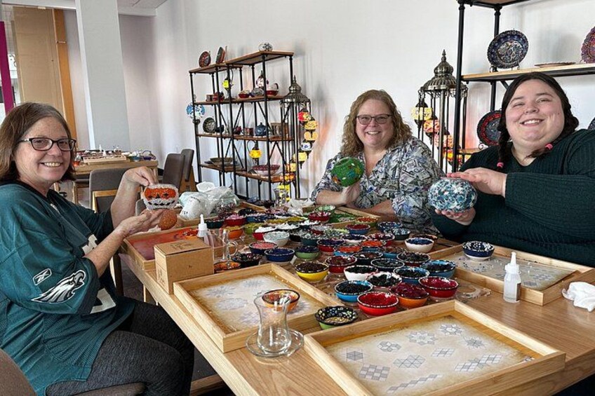 Tres personas sentadas en una mesa con varios cuencos y cerámicas de colores. 2