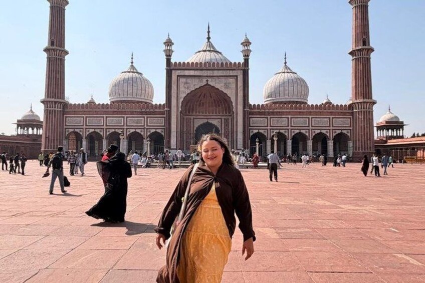 A large mosque with domes and minarets, a paved courtyard, and people walking around. 2