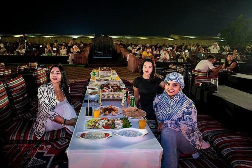Un grupo de personas cenando en un restaurante al aire libre, con una larga mesa dispuesta con diversos platos y bebidas. 2