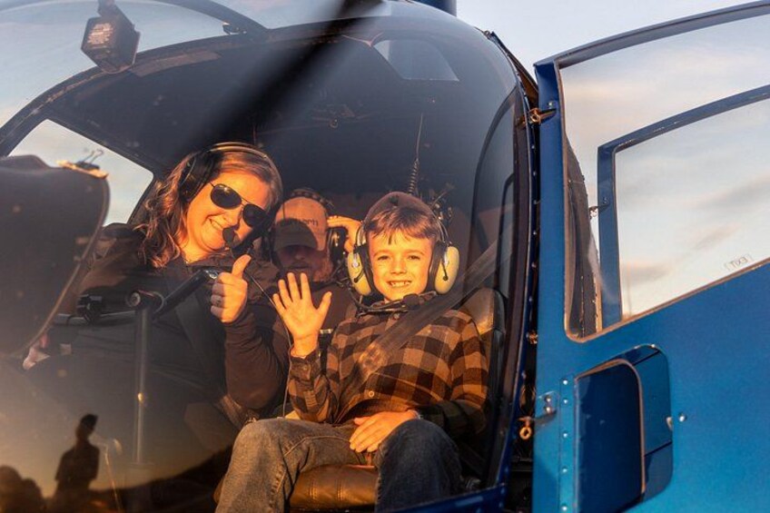 A helicopter with three people inside, one giving a thumbs up. 2
