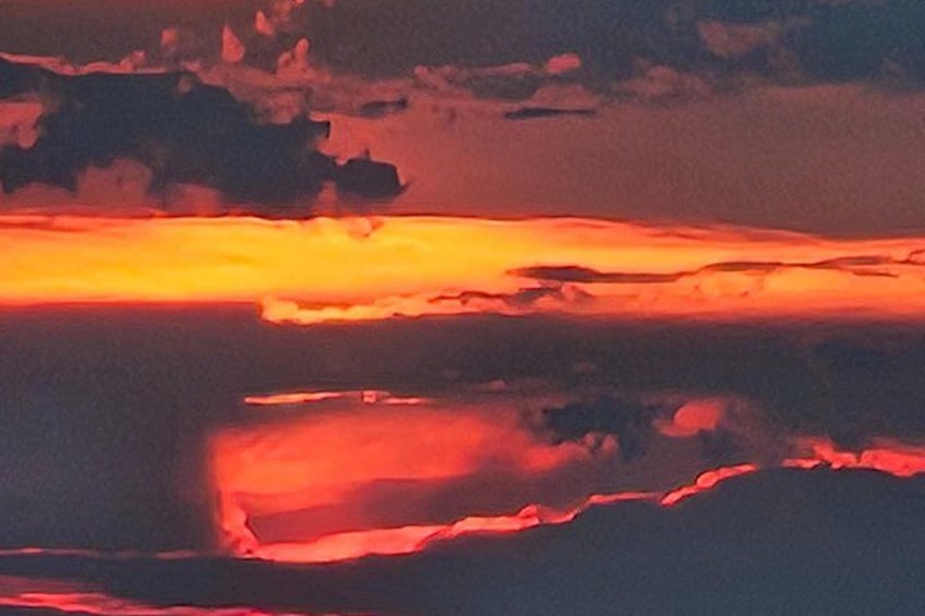 En solnedgång över en vattenyta, där molnen speglar himlens orange och röda färger. 5