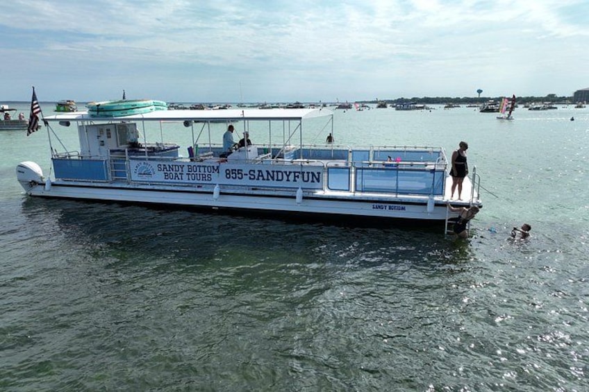 Un bateau appelé « Sandy Bottom Boat Tours », portant le numéro 855-SANDYFUN sur sa coque, flotte sur une eau calme sous un ciel dégagé. 3
