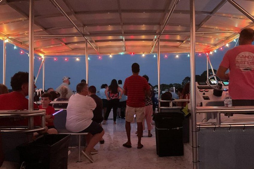 Un espace extérieur abrité où des personnes sont assises à des tables, avec des guirlandes lumineuses et un bateau dont une personne est aux commandes. 5