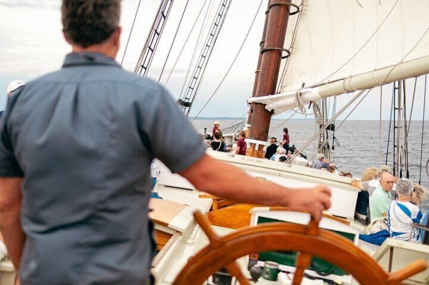 A person steering a sailboat with passengers on deck. 4