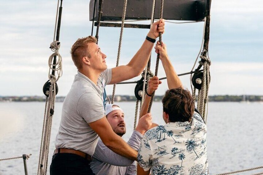 Three people on a sailboat, handling ropes and rigging. 1