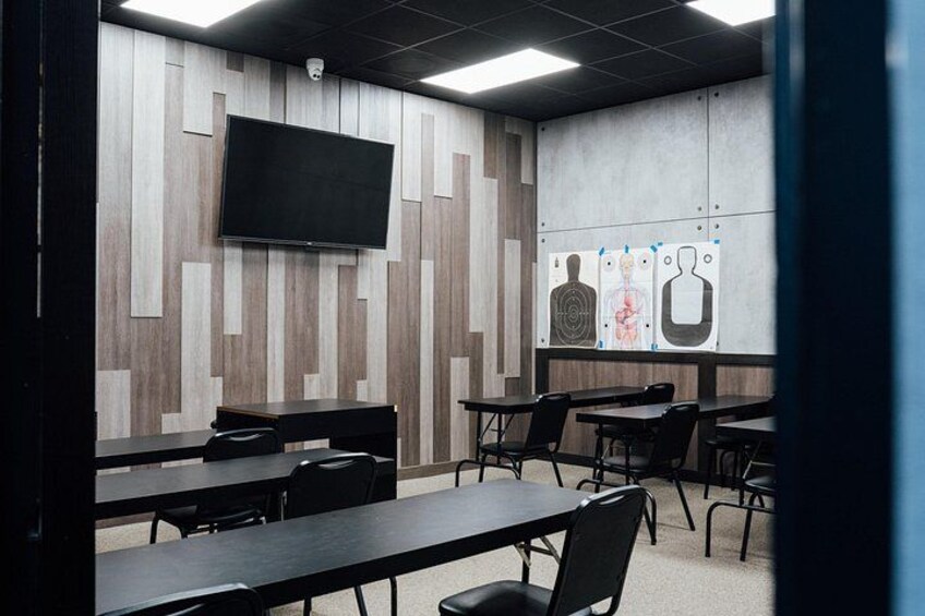 A conference room with tables, chairs, a mounted TV, and educational posters on the wall. 5