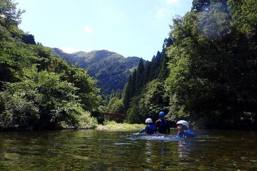 Two people kayaking on a river surrounded by dense forest and mountains. 2