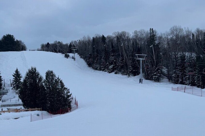 A snow-covered ski slope with trees and a ski lift. 2
