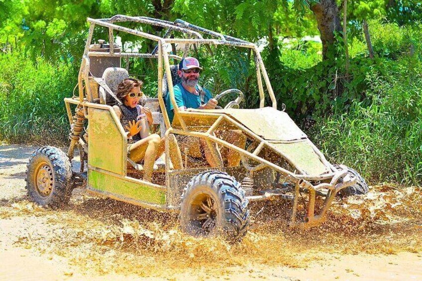 A yellow off-road vehicle driving through a muddy area with trees in the background. 4