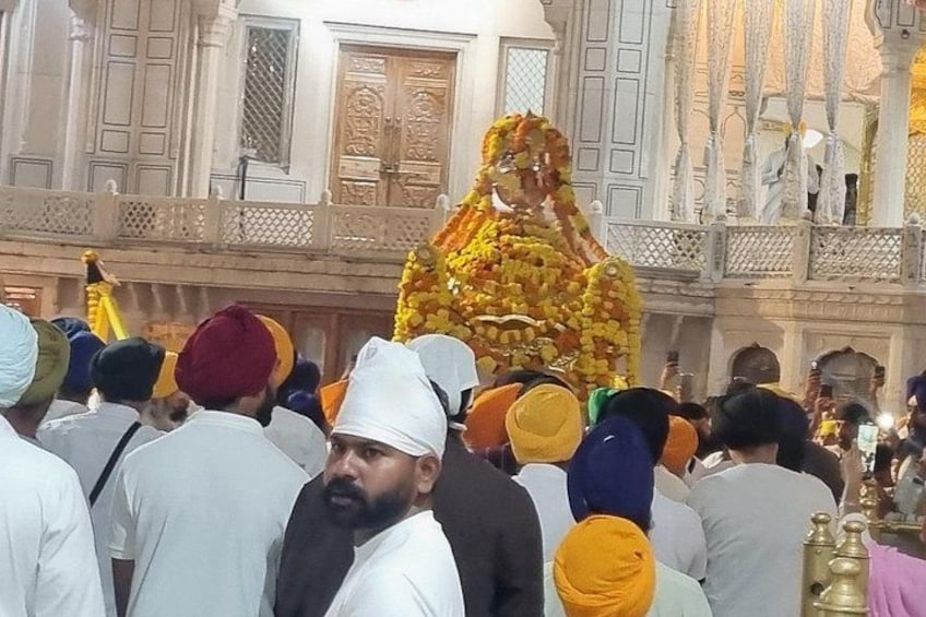 A crowd of people in traditional attire, a building with ornate architecture, and a person in a yellow turban. 2