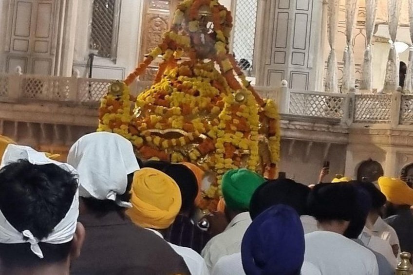 A statue adorned with flowers, surrounded by people. 3