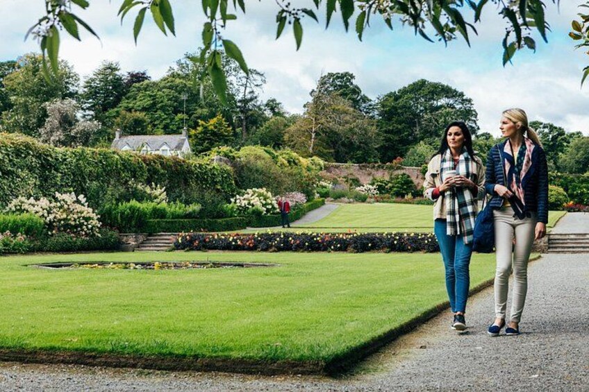 Two people walking on a pathway in a garden with manicured lawns and flower beds. 2
