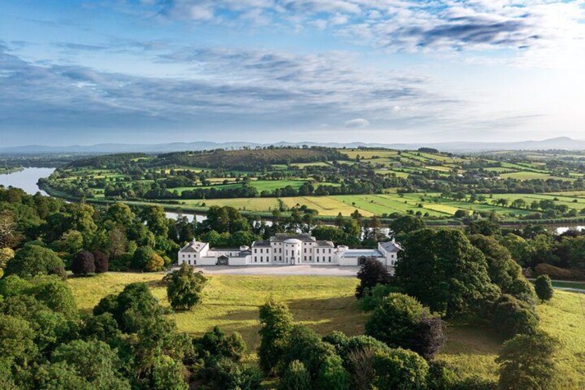 A large estate with a white building surrounded by lush greenery and a river in the background. 2