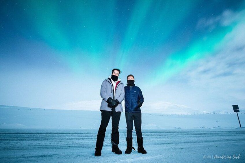 Dos personas en un paisaje nevado, con la aurora boreal de fondo. 5