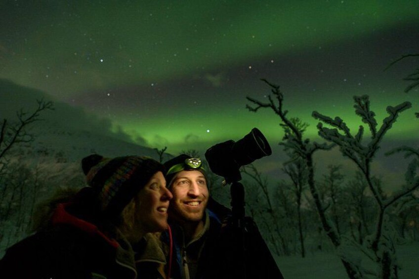 Una persona con un telescopio en un bosque nevado bajo una aurora verde. 2