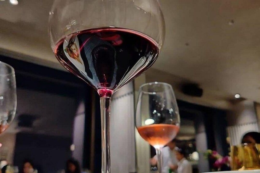 A close-up of a wine glass filled with red wine, with reflections visible on the glass surface. 5